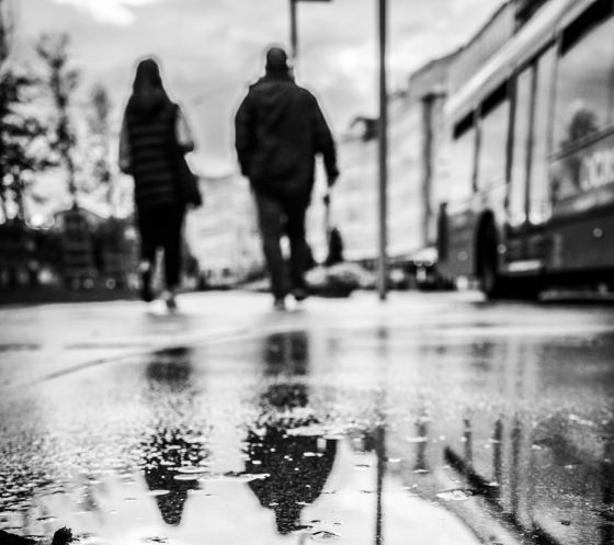 Fotografía en blanco y negro de unas personas alejándose con su silueta reflejada en un charco