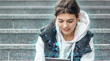 Imagen de una chica sentada en unas escaleras de la calle, mirando una tablet de la que salen unas pequeñas esferas unidas por figuras gráficas