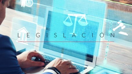 Imagen de perfil de una persona escribiendo en un ordenador portátil y donde se lee encima la palabra "legislación" junto al icono de una balanza y un mazo de juez