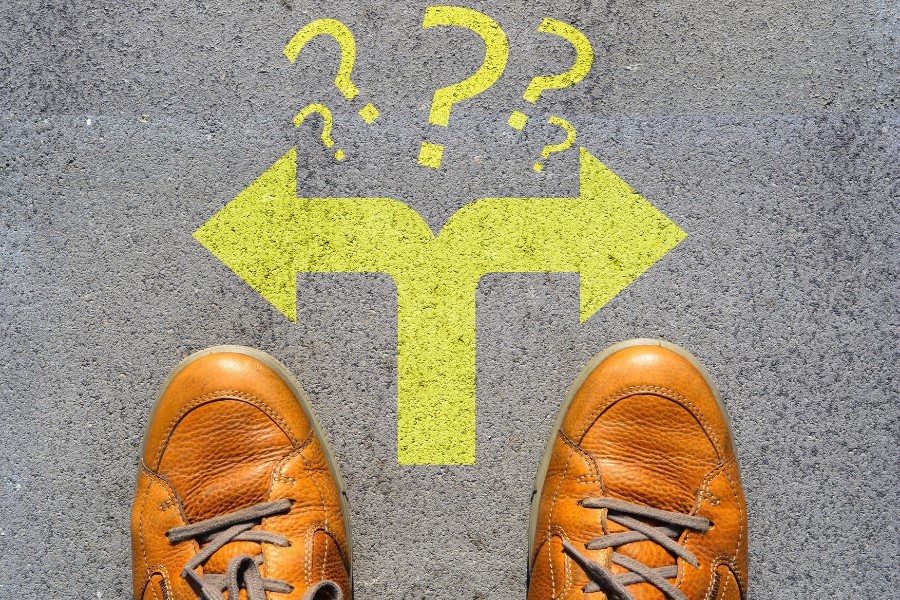 Imagen con los pies de una persona ante una flecha indicando dos direcciones y signos de interrogación.