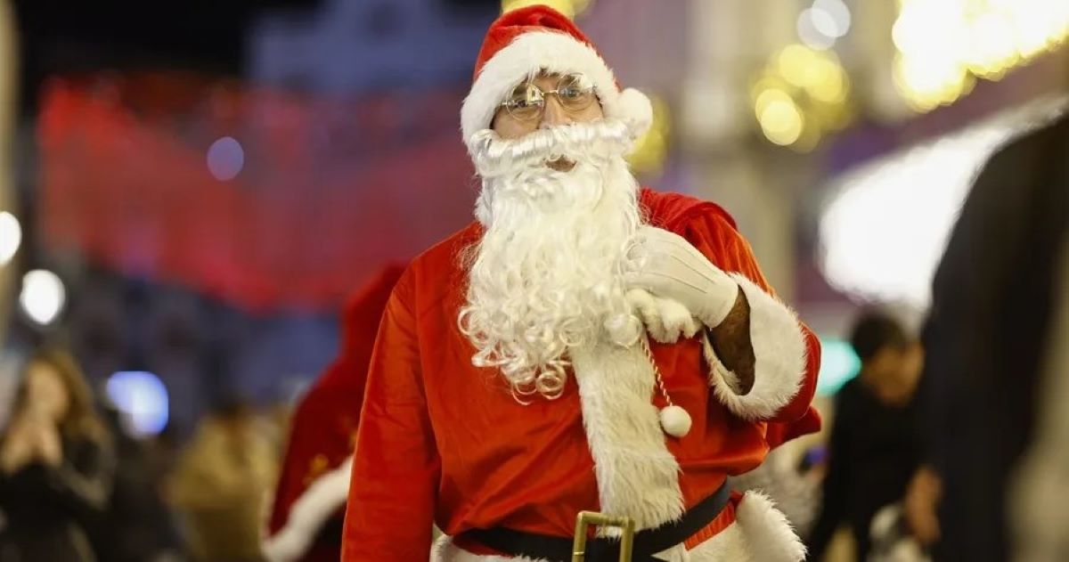 Persona disfrazada de Papa Noel con el fondo difuminado. Se aprecia que está en una calle llena de gente y es de noche.